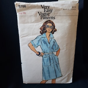Pode incluir: Envelope de padrão de costura Vintage Vogue Patterns. A ilustração mostra uma mulher em um vestido azul claro com mangas curtas, gola e cinto. O envelope é branco sujo com o texto "Very Easy Vogue Patterns" e o tamanho é 16.