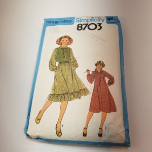 May include: Vintage Simplicity 8703 sewing pattern. The pattern envelope shows illustrations of two dresses. One dress is green with a vest, and the other is red. The envelope is blue and white with the text "Simplicity 8703".