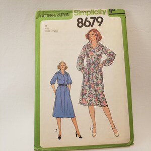 May include: Simplicity sewing pattern number 8679 for a dress. The pattern is for misses sizes 12. The pattern shows two models wearing the dress. One model is wearing a blue dress with a belt and the other model is wearing a floral print dress with a belt.