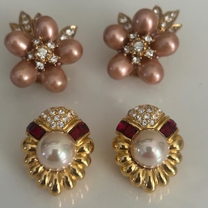 May include: Four pairs of earrings. Two pairs are flower-shaped with pink pearl-like petals and gold accents. The other two pairs are gold with a large pearl center, red accents, and a crystal-studded top.