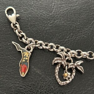 May include: Silver charm bracelet with two charms: a Florida-shaped charm with a floral design and a palm tree charm with a gold-colored center. The bracelet has a lobster clasp.