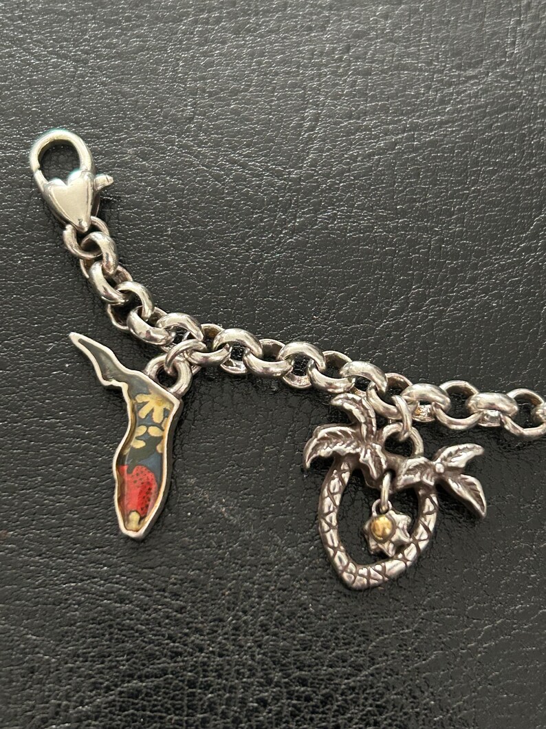 May include: Silver charm bracelet with two charms: a Florida-shaped charm with a floral design and a palm tree charm with a gold-colored center. The bracelet has a lobster clasp.
