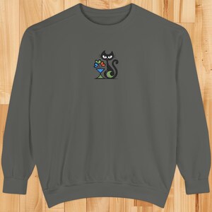 May include: A charcoal gray sweatshirt featuring an embroidered black cat design. The cat is sitting next to a martini glass with colorful hearts. The long-sleeved top is made of a soft material.