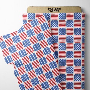 Puede incluir: Tela blanca con un patrón repetido de cuadrados de banderas americanas rojas, blancas y azules. La tela está doblada por la mitad y las palabras "PATTERN HAPPY" están impresas en una etiqueta marrón.