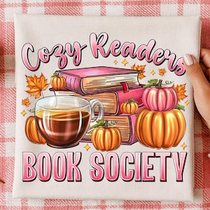 Peut inclure: Un carré de tissu blanc avec une impression graphique portant le texte "Cozy Readers BOOK SOCIETY" en rose. L'illustration comprend une pile de trois livres, une tasse en verre remplie d'un liquide brun, ainsi que plusieurs citrouilles et feuilles.