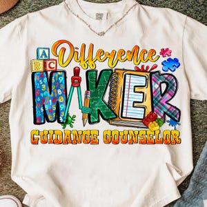 May include: White t-shirt featuring a vibrant graphic with the text "Difference Maker Guidance Counselor." The design incorporates ABC blocks, numbers, a compass, a pencil, a notebook, and puzzle pieces.