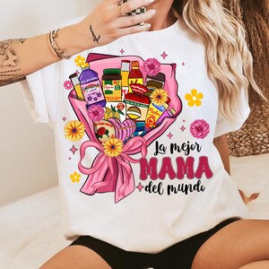 May include: White t-shirt with a pink and yellow floral design featuring a bouquet of various grocery items and the text "La mejor MAMA del mundo".