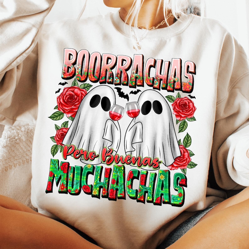 May include: White sweatshirt with a graphic design featuring two ghost figures holding wine glasses. The text "Borrachas Pero Buenas Muchachas" is displayed in a colorful, floral font, with red roses and green leaves.
