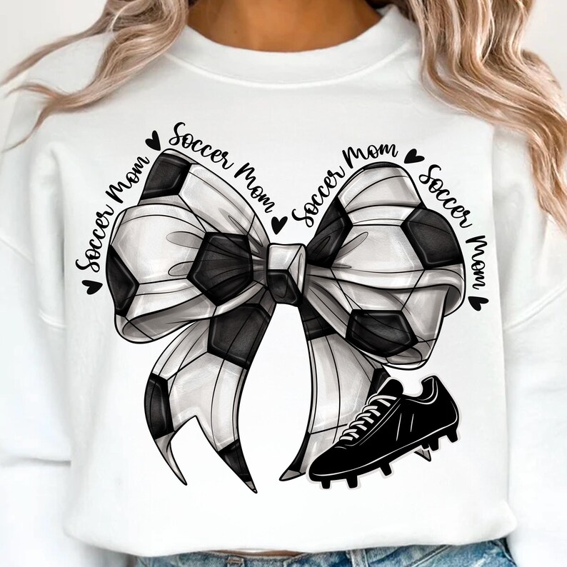 May include: White sweatshirt with a black and white soccer ball bow design and a black soccer cleat. The words "Soccer Mom" are written around the bow in a circular pattern. A cute and sporty design.