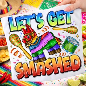 Puede incluir: Camiseta blanca con un gráfico colorido que presenta una piñata, maracas y un tambor. El texto "LET'S GET SMASHED" se muestra en colores vibrantes y degradados. El diseño es festivo y divertido, perfecto para una celebración.