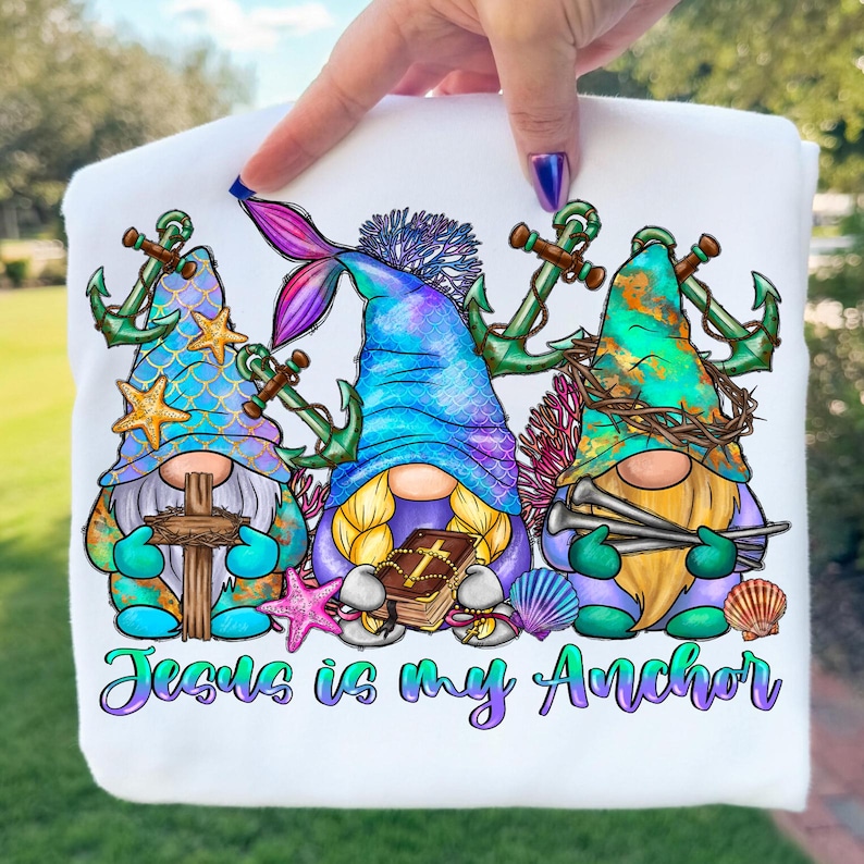 May include: White sweatshirt featuring three gnome characters with nautical and religious themes. The gnomes have anchors, crosses, and a mermaid tail. The text "Jesus is my Anchor" is written in teal script at the bottom.