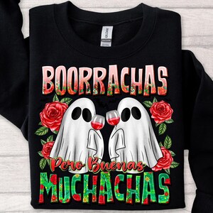 May include: Black sweatshirt with the words "BOORRACHAS Pero Buenas MUCHACHAS" in a floral design. Two white ghost figures are holding wine glasses, surrounded by red roses. A fun, festive design.