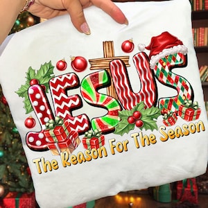May include: White Christmas-themed pillow with the word "JESUS" in festive lettering. The design includes a cross, holly, ornaments, and gift boxes. The text "The Reason For The Season" is also present.