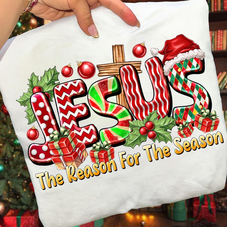 May include: White Christmas-themed pillow with the word "JESUS" in festive lettering. The design includes a cross, holly, ornaments, and gift boxes. The text "The Reason For The Season" is also present.