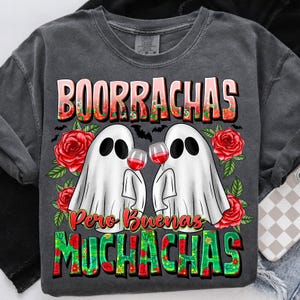 May include: Dark gray t-shirt with a graphic featuring two ghost figures toasting wine glasses. The shirt has the text "BOORRACHAS Pero Buenas MUCHACHAS" in a colorful, floral design. Red roses and bats decorate the design.