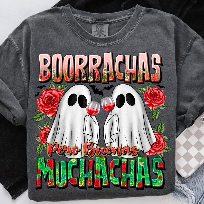 May include: Dark gray t-shirt with a graphic featuring two ghost figures toasting wine glasses. The shirt has the text "BOORRACHAS Pero Buenas MUCHACHAS" in a colorful, floral design. Red roses and bats decorate the design.