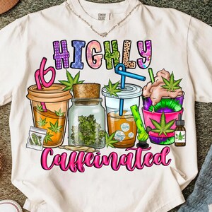 以下が含まれることがあります： 「HIGHLY」と「Caffeinated」の文字が描かれた、カラフルなグラフィックデザインの白いTシャツ。デザインには、飲み物、瓶、小さなバッグのイラストが含まれており、すべて緑色の大麻の葉で飾られています。