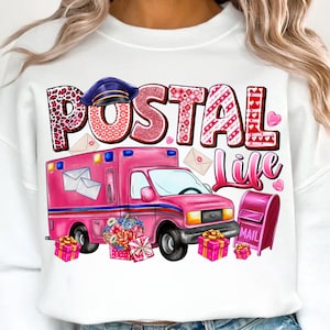 May include: White sweatshirt with a graphic design featuring a pink postal truck, mailboxes, and the words "POSTAL LIFE." The design includes a postal hat, hearts, and gift boxes, creating a themed design.