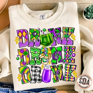 May include: A white sweatshirt with a colorful graphic design that says "DRINK DRINK DRINK". The graphic features purple, green, yellow, and black colors and includes a Mardi Gras mask and two glasses of purple and green drinks.