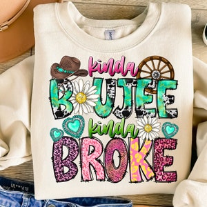 May include: A beige sweatshirt with the text "kinda boujee kinda broke" in pink, green, and black lettering. The text is decorated with cow print, leopard print, hearts, and flowers.