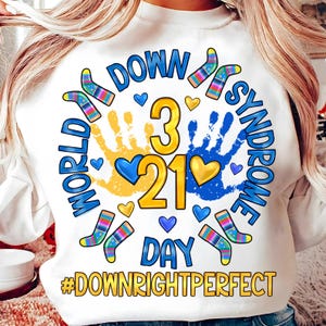Pode incluir: Camisola branca com um design gráfico colorido que diz "Dia Mundial da Síndrome de Down" com a data "3.21" e a hashtag "#Downrightperfect".