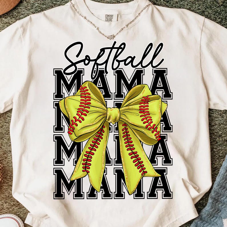 May include: White t-shirt with a large graphic featuring the words "Softball MAMA" in black block letters. A yellow bow, designed to resemble a softball, is centered on the shirt, with red stitching details.