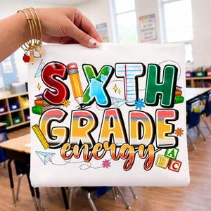 Pode incluir: Uma bolsa de tecido branco com o texto colorido "SIXTH GRADE energy" e ilustrações gráficas de um lápis, um globo, papel pautado, uma régua, aviões de papel e blocos do alfabeto. O design utiliza as cores vermelho, amarelo, azul e verde.