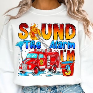 May include: White sweatshirt with a red fire engine, flames, and the text "Sound the Alarm I'm 3".