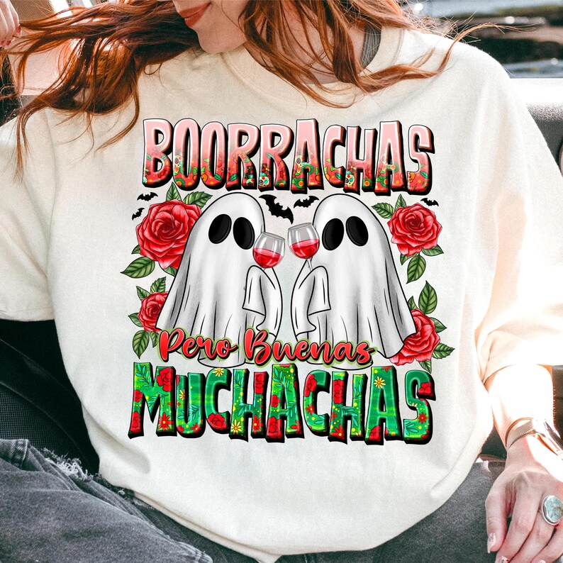 May include: White sweatshirt featuring a graphic of two ghost figures holding wine glasses. The text "BOORRACHAS Pero Buenas MUCHACHAS" is displayed above and below the ghosts, with red roses and bats as decorative elements.