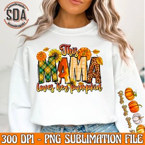 May include: White sweatshirt with a graphic design featuring the text "This Mama loves her pumpkin" in a patchwork style with fall colors and images of pumpkins, sunflowers, and leaves.