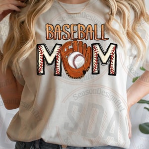 K&ouml;nnte beinhalten: Wei&szlig;es T-Shirt mit dem Text "Baseball Mom" in braunen und roten Buchstaben. Ein Baseballhandschuh mit einem Baseball darin befindet sich in der Mitte des Textes.