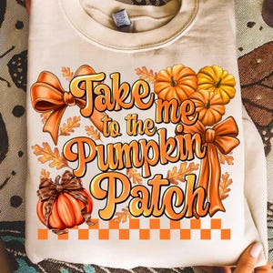 以下が含まれることがあります： クリーム色のスウェットシャツ。オレンジと黄色の「Take me to the Pumpkin Patch」の文字。オレンジ色のカボチャ、リボン、秋の葉のデザインで、オレンジと白のチェック柄のボーダーが付いています。