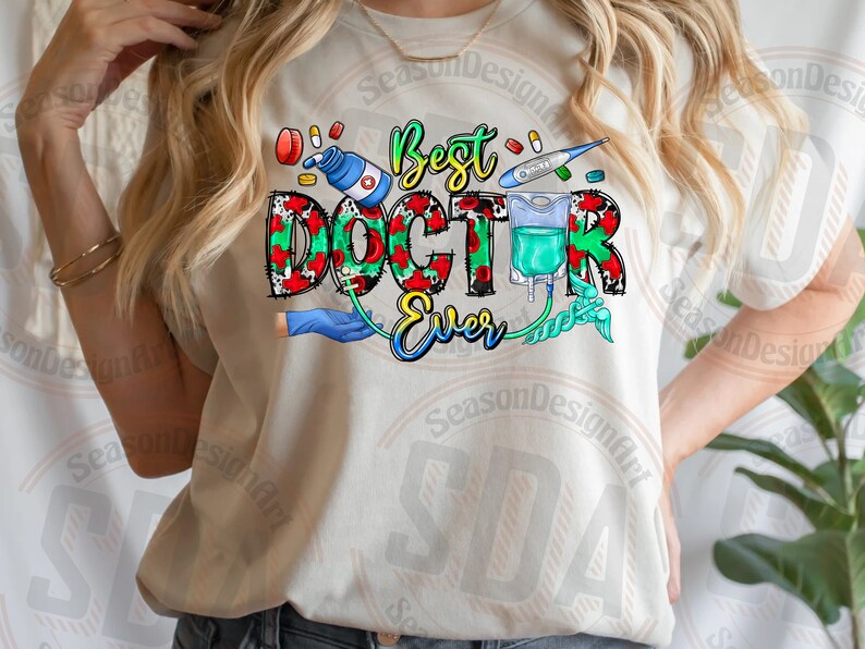 K&ouml;nnte beinhalten: Wei&szlig;es T-Shirt mit einem bunten Grafikdesign, auf dem "Best Doctor Ever" steht. Das Design enth&auml;lt ein Stethoskop, ein Thermometer, eine Pillenflasche und eine Infusionstasche.