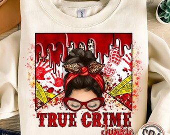 May include: A white sweatshirt with a graphic design of a woman with red hair and glasses. The graphic includes red blood splatters, yellow crime scene tape, and the text "TRUE CRIME Junkie".