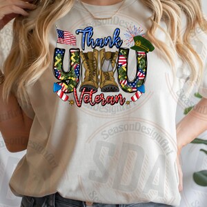 May include: White t-shirt with a graphic design that says "Thank You Veteran" with a camouflage pattern, an American flag, boots, and fireworks.