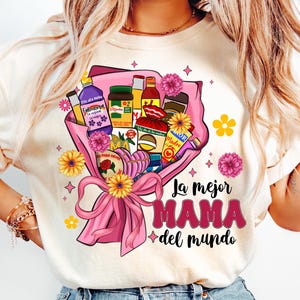 May include: A white t-shirt with a pink and yellow floral design. The design features a bouquet of various Mexican grocery items, including a bottle of Fabuloso, a jar of Mama brand salsa, and a box of La Banderita tortillas. The text "La mejor MAMA del mundo" is printed below the bouquet.