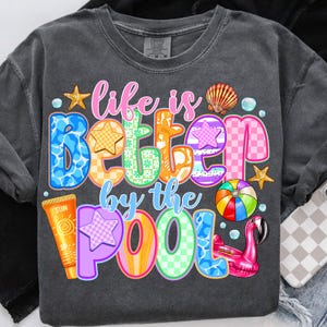 May include: A dark grey t-shirt with the text "Life is better by the pool" in colorful letters. The letters are decorated with a variety of summer-themed designs, including a seashell, a starfish, a flamingo, a beach ball, and a bottle of sunscreen.