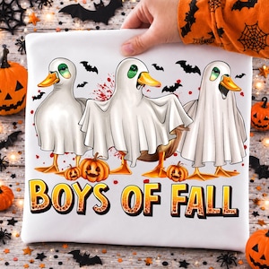May include: A white t-shirt featuring a graphic of three ducks wearing white ghost costumes. The design includes small orange pumpkins, black bats, and red splatters. The text BOYS OF FALL is printed in large, bold, orange and black gradient letters.