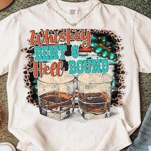 Könnte beinhalten: Weißes T-Shirt mit dem Text "Whiskey Bent & Hell Bound" in orange und türkis. Das Design umfasst zwei Whiskeygläser und ein türkisfarbenes und Leopardenmuster.
