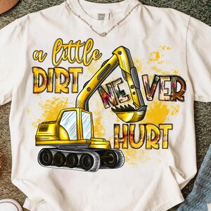 May include: White t-shirt with a yellow excavator graphic and the text "a little dirt never hurt" in a playful font. The excavator is detailed with black and gray accents, and the text has a watercolor effect.