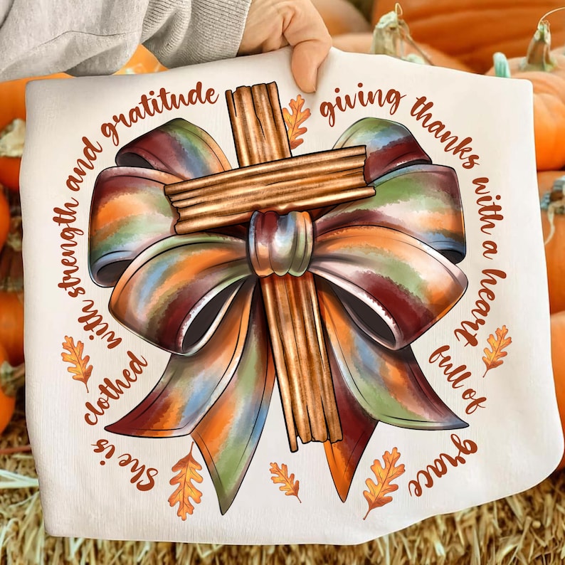 May include: A cream-colored decorative pillow featuring a cross made of cinnamon sticks and a large, colorful bow. The text around the bow reads "She is clothed with strength and gratitude, giving thanks with a heart full of grace."