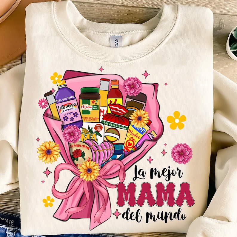 May include: A white t-shirt with a pink and yellow bouquet of flowers and various food items. The text "La mejor MAMA del mundo" is printed in red and pink on the shirt.