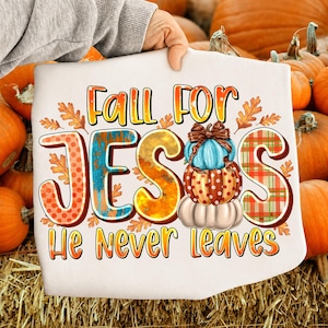 May include: A white t-shirt featuring the text Fall For JESUS He Never leaves in orange and yellow gradient lettering. The letter U is replaced by a stack of three pumpkins in blue, orange with white dots, and cream, accented by autumn leaves.