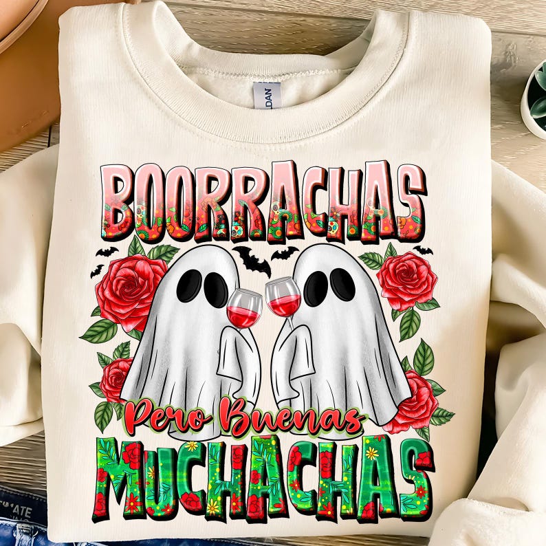 May include: Cream-colored sweatshirt with a graphic featuring two white ghost figures holding wine glasses. The text "BOORRACHAS Pero Buenas MUCHACHAS" is displayed in a colorful, floral design, with red roses and bats.