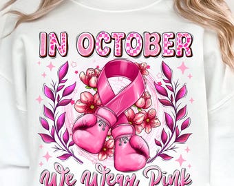 May include: White sweatshirt with a pink ribbon, boxing gloves, and floral design. The text "IN OCTOBER" and "we wear Pink" are displayed in pink. The design is for breast cancer awareness.