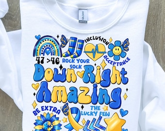 May include: White sweatshirt with a colorful graphic design featuring the text "Down Right Amazing" and other related phrases like "Rock Your Sock", "Inclusion", "Acceptance", "The Lucky Few", and "3/21 Awareness".