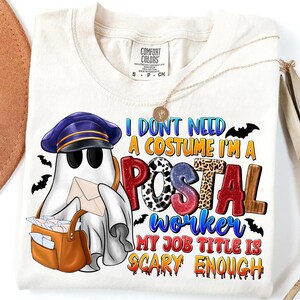 May include: Cream-colored t-shirt with a graphic of a ghost dressed as a postal worker, holding a mailbag and letters. The text reads "I DON'T NEED A COSTUME I'M A POSTAL WORKER MY JOB TITLE IS SCARY ENOUGH". Includes bats.