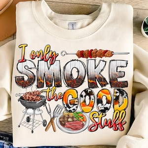 Può includere: Una felpa bianca con il testo "I only smoke the good stuff" in lettere nere, rosse e gialle. Il testo è circondato da immagini di una griglia, spiedini e cibo.