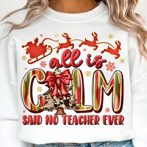 Op de afbeelding: Witte sweatshirt met een kerstthema. Het ontwerp toont de slee van de kerstman, rendieren, sneeuwvlokken en de woorden "all is calm" met een kerstboom en een strik. De zin "said no teacher ever" is ook opgenomen.