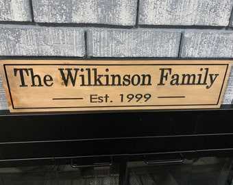 May include: A rectangular light brown wooden sign with a black border and black engraved text that reads The Wilkinson Family Est. 1999. The sign features a smooth finish and is positioned horizontally with clear, dark lettering.